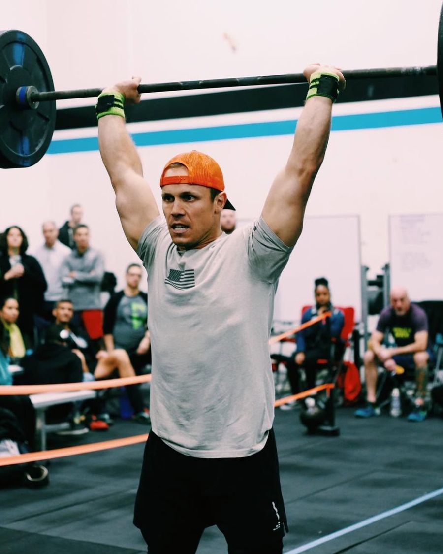 A masters athlete pressing a barbell overhead in front of a crowd at a Garage Games competition